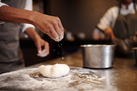 Closeup image of baker adding pinch of flour to kneaded doughの写真素材