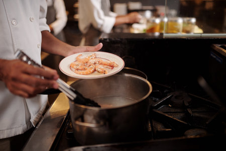 Cook taking boiled prawns from saucepan and putting on plateの写真素材