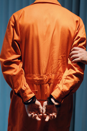 Police officer walking arrested criminal in orange uniform to jail, view from backの写真素材