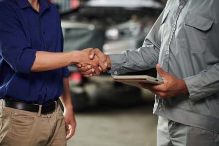 Mechanic and car owner shaking hands and signing documentの写真素材