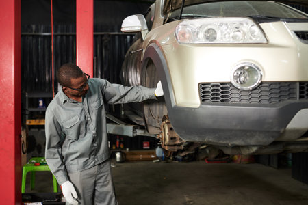 Car mechanic in grey overall examining suspended carの写真素材