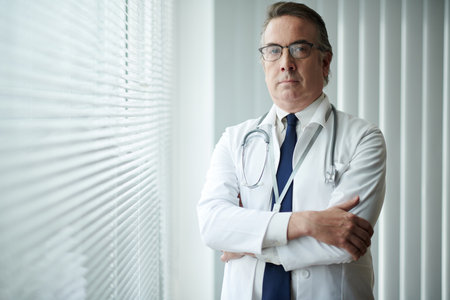 Portrait of serious confident general practitioner standing at window in medical officeの写真素材