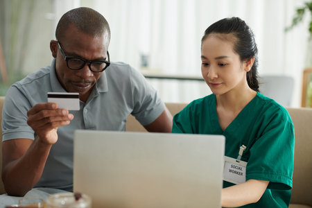 Social worker visiting patient at home and teaching him to order food deliveryの写真素材