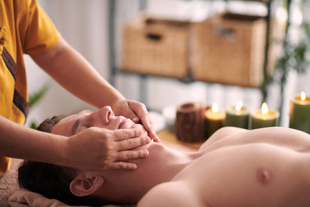 Beautician giving young man rejuvenating face massage to reduce appearance of wrinkles and fine lines.の写真素材