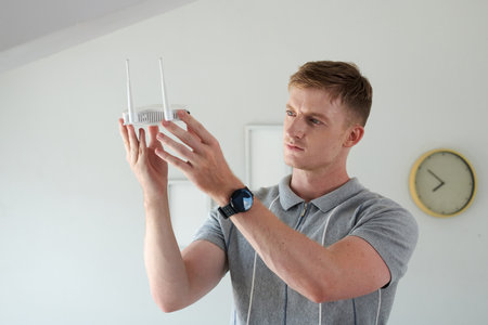 Portrait of pensive man looking at small wifi router in his handsの写真素材