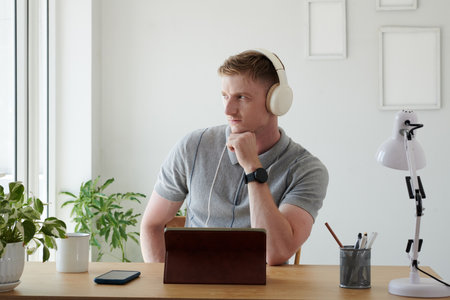Pensive businessman in headphones looking away through windowの写真素材