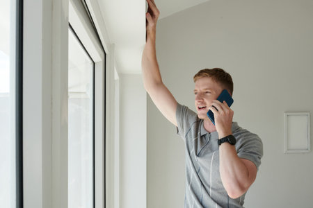 Excited young businessman looking outdoors through window and talking on phone with coworkerの写真素材