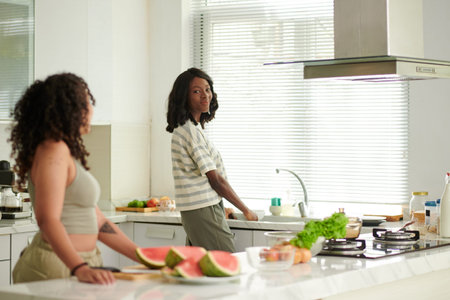 Cheerful female roommates cooking dinner in kitchen