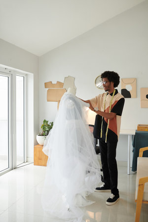 Fashion designer creating wedding dress with tulle cape for clientの写真素材