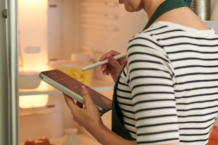Woman checking list of ingredients on tablet computer when taking products out of fridge