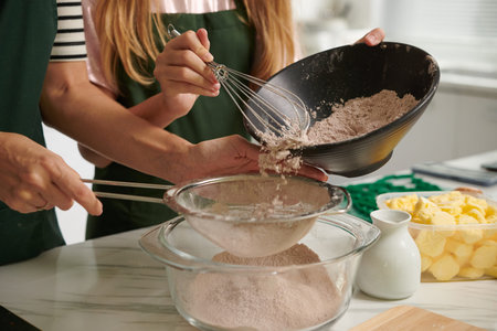 Mother and teenage daughter sifting flour and spices into big bowl