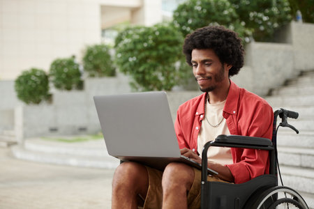 Young Black man with disability working as freelancer, he is answering e-mails on laptop