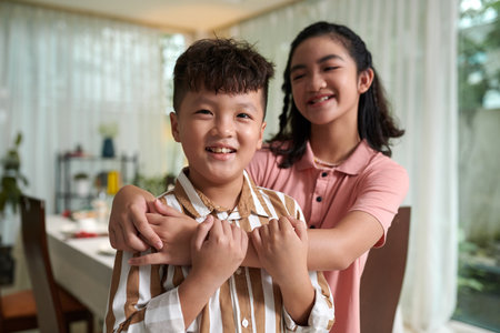 Joyful teenage girl hugging her little brother from behindの写真素材