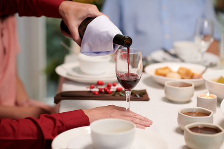 Man filling glass with red wine at family celebrationの写真素材