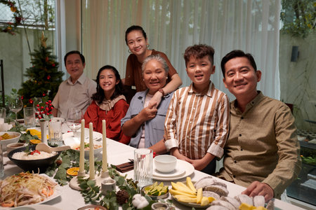 Happy big Vietnamese family sitting at dinner table served for New Year celebrationの写真素材