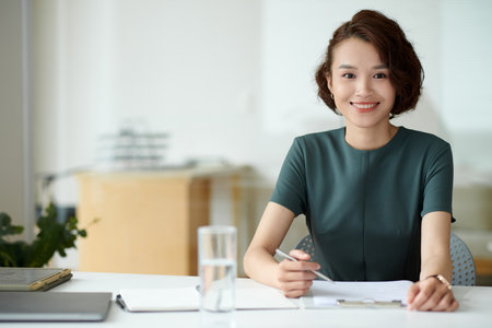 Portrait of female entrepreneur filling application form when working at office deskの写真素材