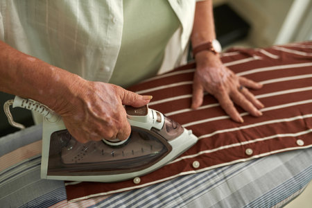 Hands of senior woman ironing cotton shirt on boardの写真素材