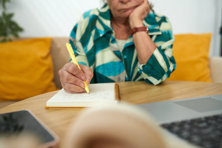 Pensive senior woman filling her gratitude journal after long dayの写真素材