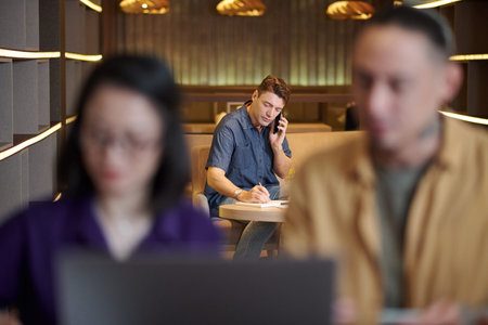Middle-aged entrepreneur making phone call to business partner and writing down ideas