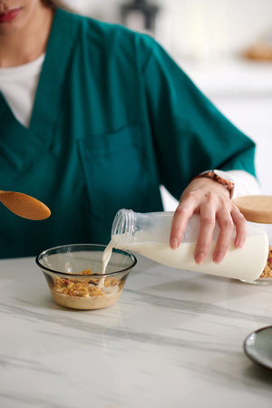 Cropped image of medical nurse adding non-dairy milk in bowl with muesli