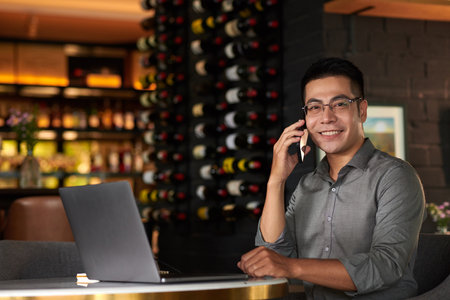 Portrait of cheerful Vietnamese entrepreneur working on laptop in his restaurantの写真素材