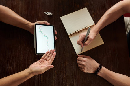 Hands of crypto traders checking uptrend line candlestick graph when working on trading planの写真素材