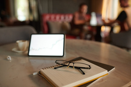 Glasses on stack of planners next to digital tablet on table in coffeeshop