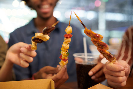 Joyful friends having meat skewers for lunch in outdoor cafeの写真素材