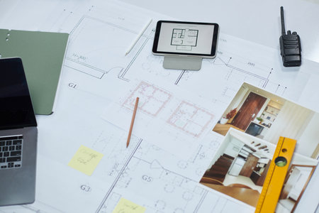 Tablet computer, photos, laptop and construction level on apartment floor blueprintの写真素材