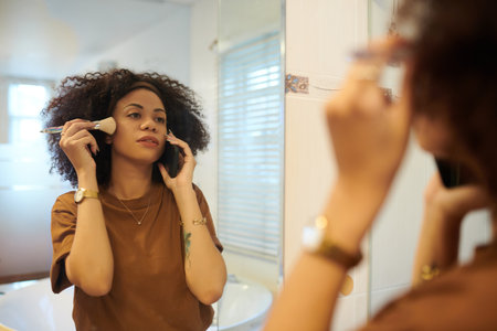 Hispanic woman talking on phone with friend and applying makeupの写真素材