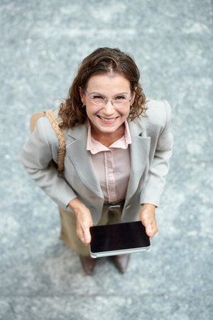 Happy middle-aged entrepreneur with digital tablet looking up at cameraの写真素材