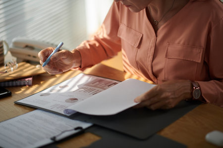 Cropped image of mature female entrepreneur analyzing information in printed report of marketing departmentの写真素材