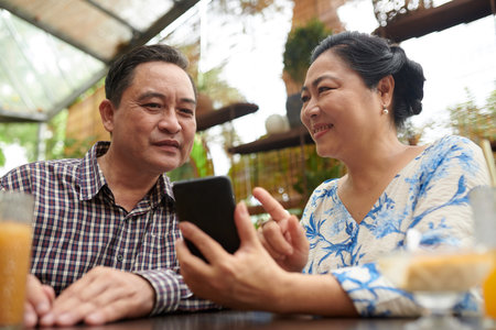Smiling senior woman showing photo on social media to husband when they are spending time in coffeeshopの写真素材