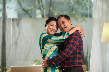 Portrait of happy elderly couple hugging and looking at cameraの写真素材
