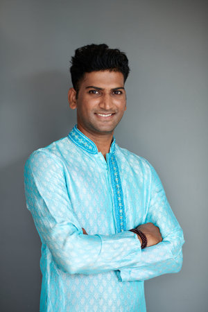 Portrait of cheerful Indian man in bright blue kurta crossing arms and smiling at camera