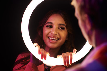 Smiling young woman looking at boyfriend through ring lightの写真素材