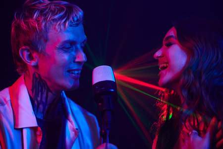 Happy young couple enjoying singing in karaoke in neon lightの写真素材