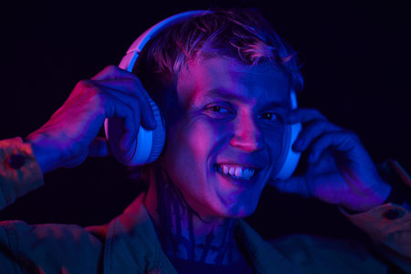Portrait of smiling man standing in neon light and putting on headphonesの写真素材