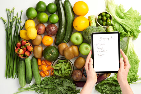 Hands of person holding tablet computer with shopping list over table with groceriesの写真素材