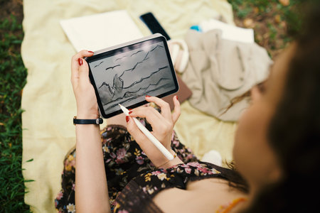 Creative young woman drawing sketch on tablet computer when resting in parkの写真素材