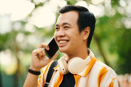 Portrait of smiling young Vietnamese man talking on phone with friend when walking outdoorsの写真素材