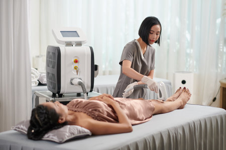 Beautician epilating legs of female client with laserの写真素材