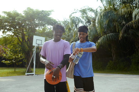 Excited Black man checking fitness tracker after spending time with friend on streetball court