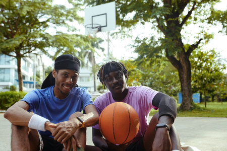 Cheerful Black men resting after playing streetball together after workの写真素材