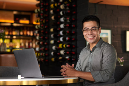Portrait of smiling entrepreneur working on laptop at table in restaurantの写真素材