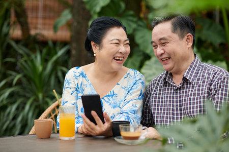 Senior Vietnamese couple laughing at post on social mediaの写真素材