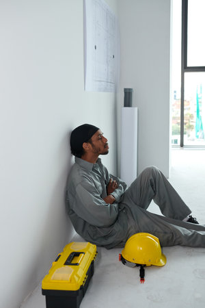 Tired builder leaning on wall when resting during short break at construction siteの写真素材