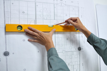 Hands of builder using construction level when measuring line on construction planの写真素材
