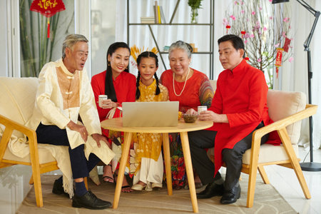 Big family gathered in front of laptop to watch movie and have some tea with treats after celebrating Spring festivalの写真素材