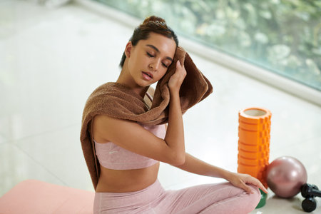 Tired young woman wiping off sweat after intense workoutの写真素材